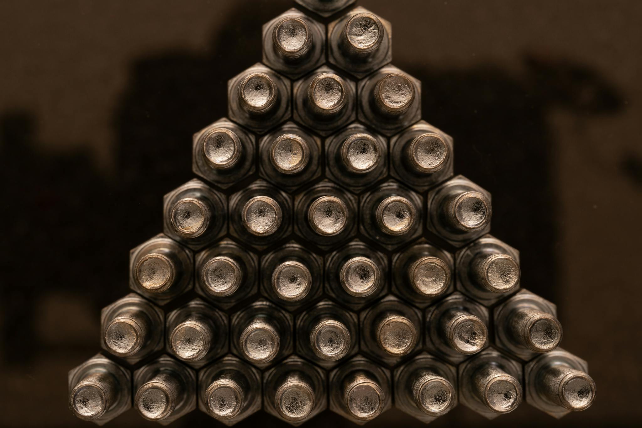 Close-up view of metallic nuts arranged in a triangular shape with a reflective surface.